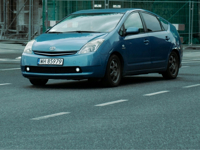 a blue car driving down a street next to a tall building