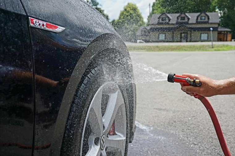 man cleaning black car wheel with hose