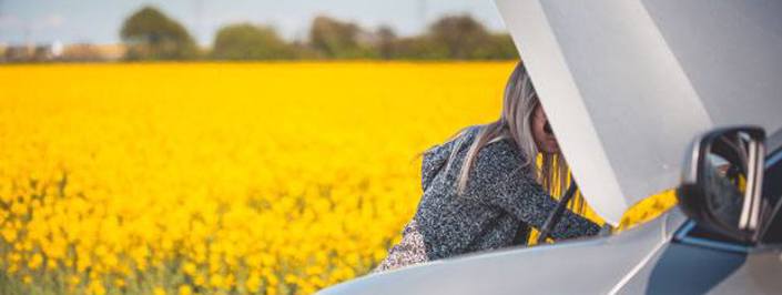 Woman trying to fix car problem with the bonnet open next to a field of sunflowers