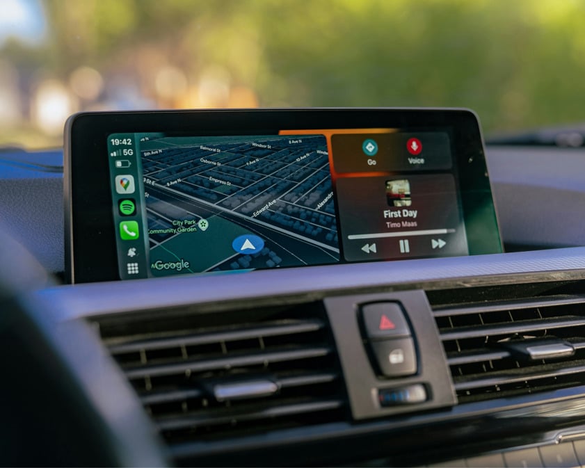 Close-up of a car dashboard showing Google Maps navigation with music controls on an infotainment screen using Apple CarPlay