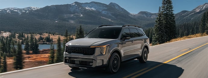 Kia Sorento driving on a mountain road with forest and lake scenery in the background