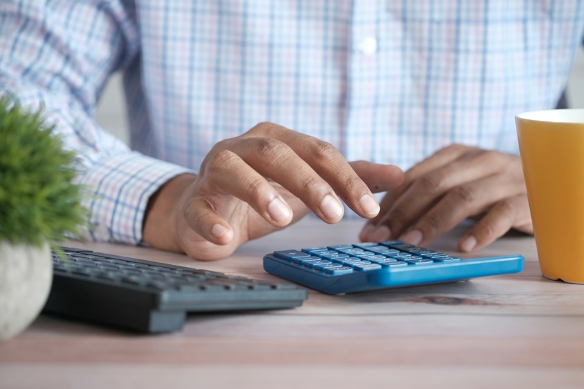 person using a calculator at desk with coffee mug