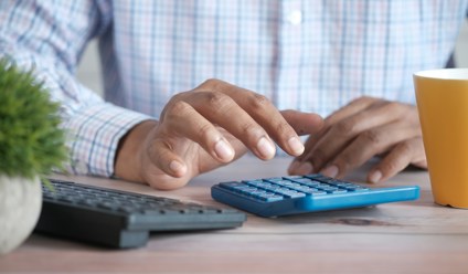 person using a calculator at desk with coffee mug