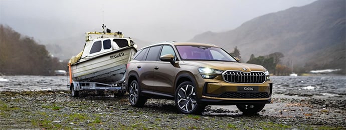 Skoda Kodiaq towing a small boat named by a lake with misty hills in the background