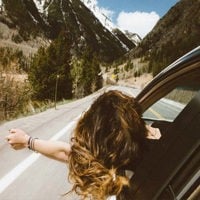 woman riding in vehicle putting her head and right arm outside the window while travelling the road