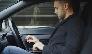 man working on laptop inside a car